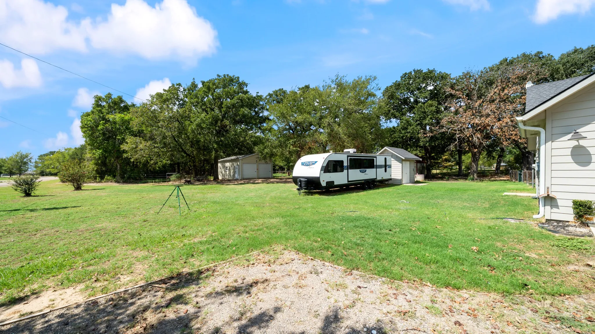 Expansive lawn area with mature trees and a detached storage structure