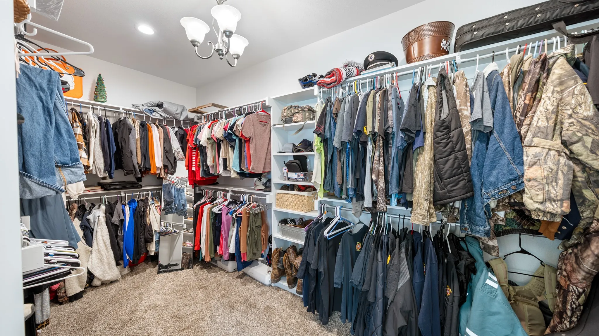 Carpeted walk-in closet featuring white shelving, multiple hanging rods, and a ceiling-mounted light fixture