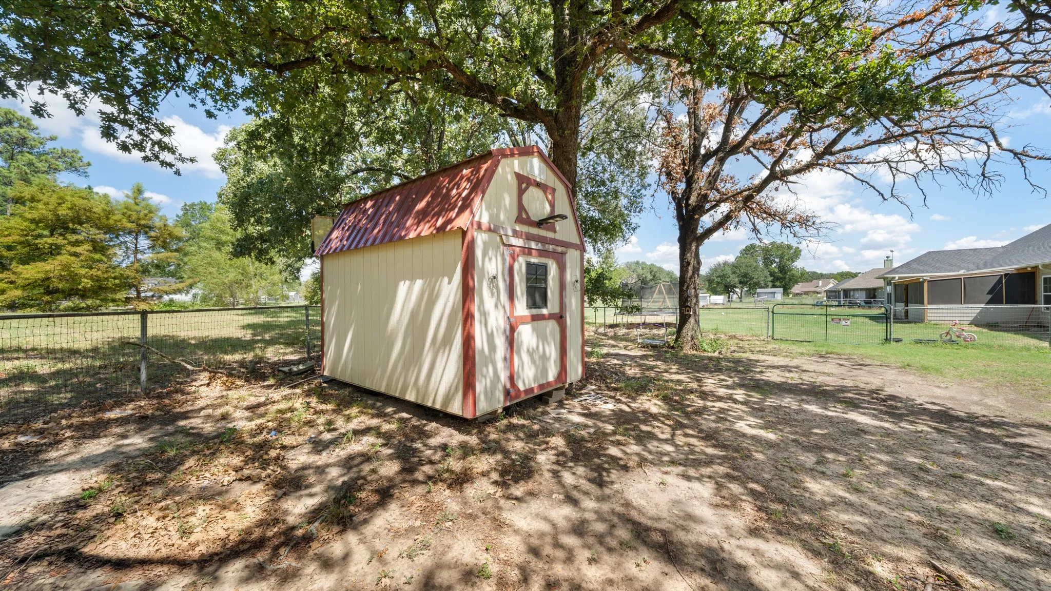Detached storage shed with a red metal roof and trim, featuring a side window