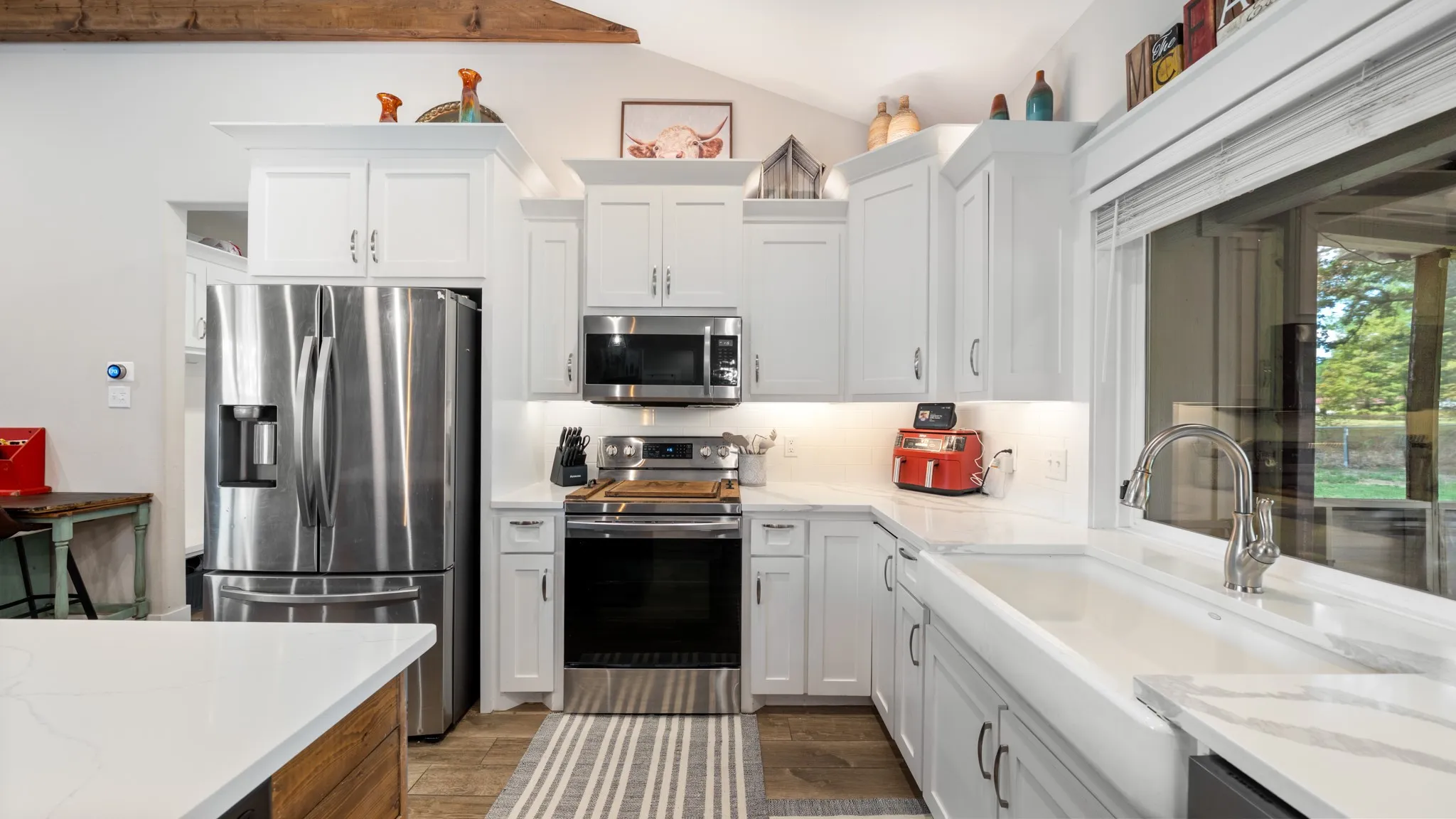 White shaker cabinetry with under-cabinet lighting, stainless steel appliances, a farmhouse-style sink, and light-toned countertops