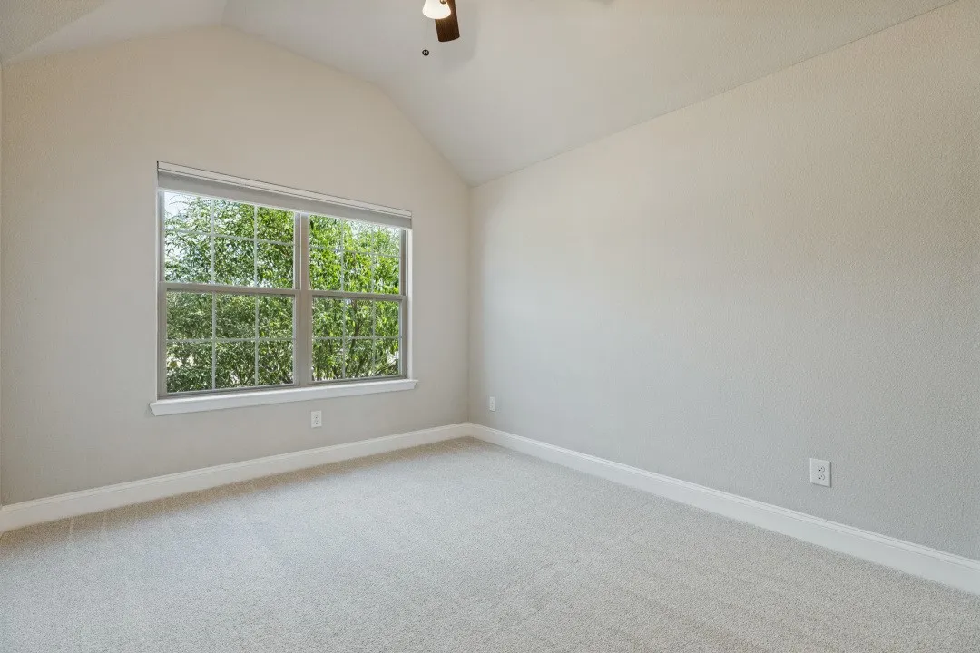 Vaulted ceiling, ceiling fan, large window with natural light, light-toned carpet, and neutral wall tones