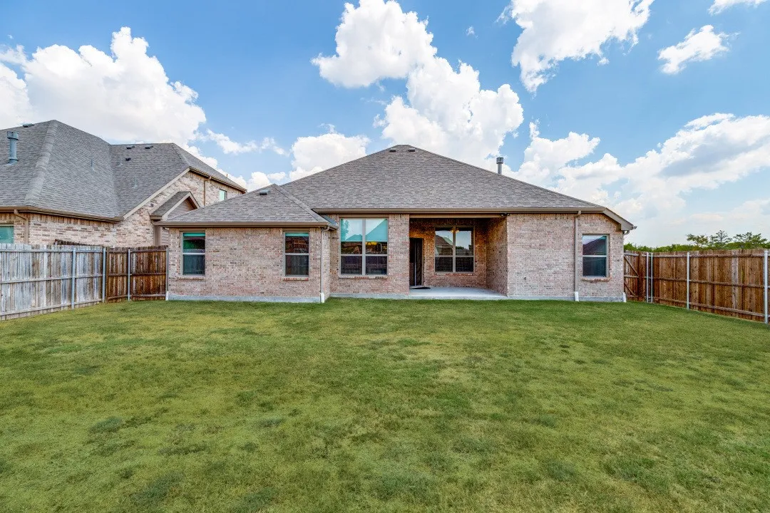 Expansive backyard featuring a manicured lawn, brick exterior, fenced perimeter, and a concrete patio