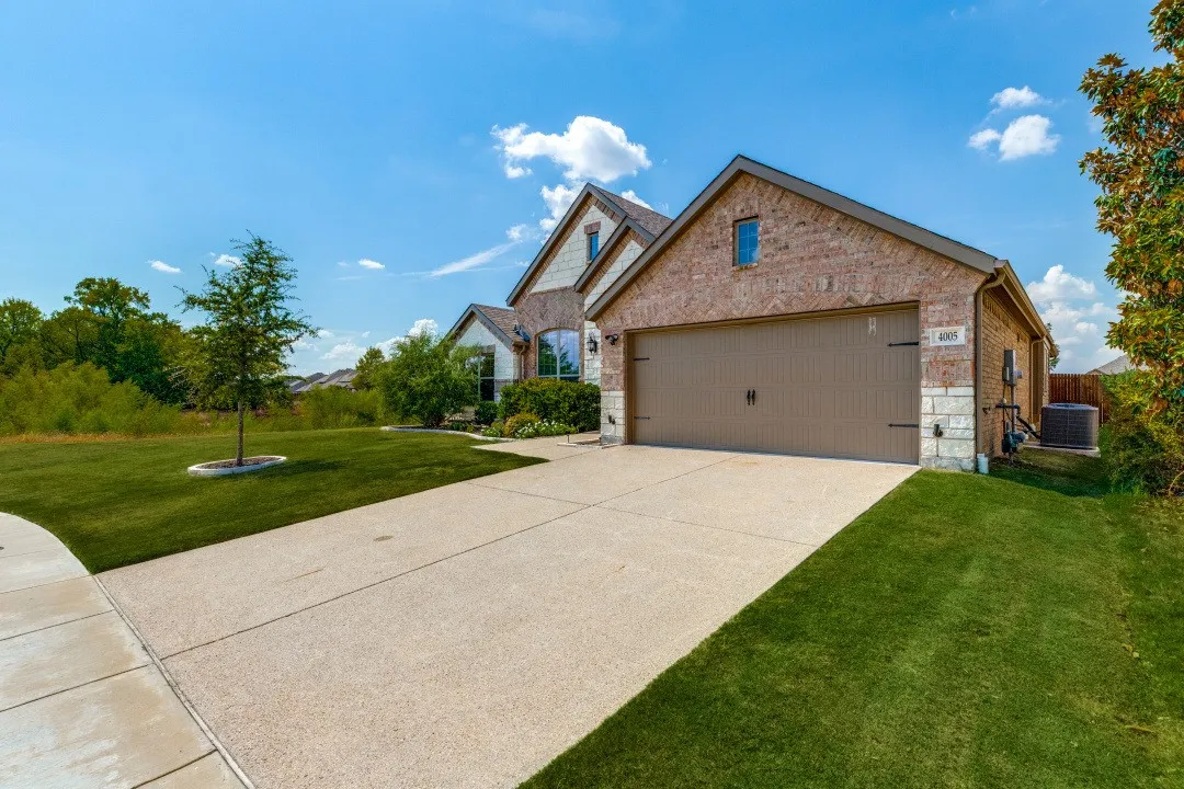 Brick and stone facade, attached garage, concrete driveway, and well-maintained lawn