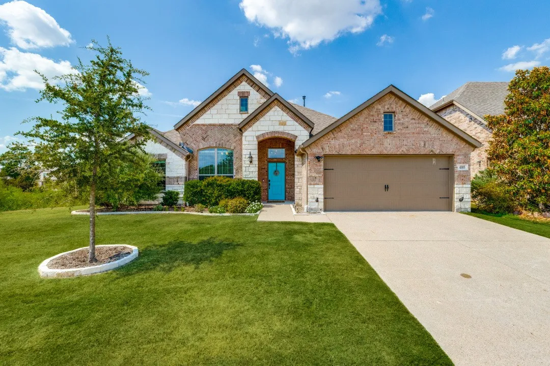 Brick and stone exterior with an attached garage, paved driveway, and mature landscaping
