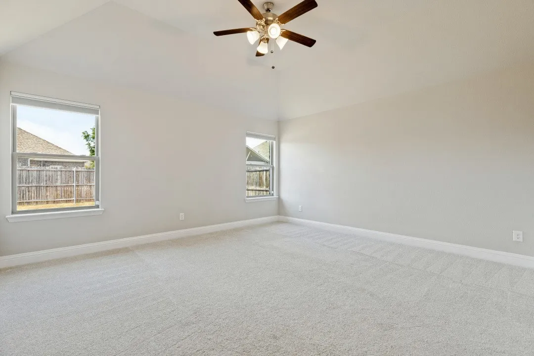 Vaulted ceiling with a ceiling fan, light-toned carpeting, and multiple windows