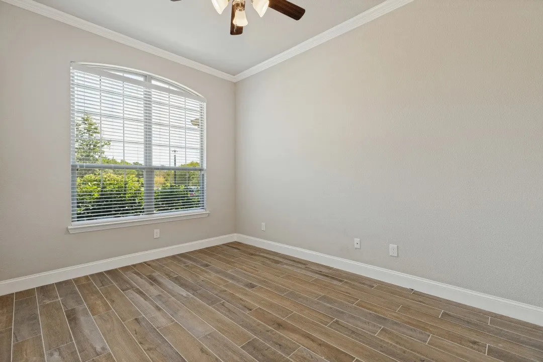 Arched window with blinds, wood-finish flooring, ceiling fan, and crown molding
