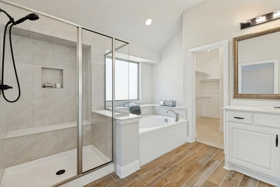 Walk-in shower with a built-in bench and recessed niche, soaking tub with window, wood-finish flooring, and a white vanity with a framed mirror