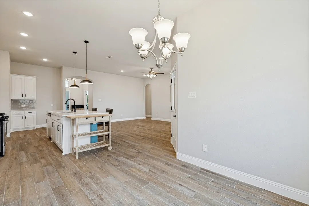 Kitchen island with integrated sink, wood-finish flooring, recessed lighting, white cabinetry, and brushed nickel chandelier