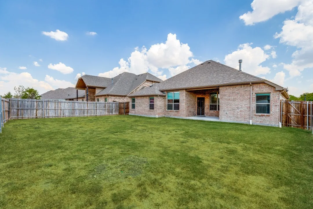 Expansive backyard featuring a manicured lawn, full privacy fencing, and a covered patio area
