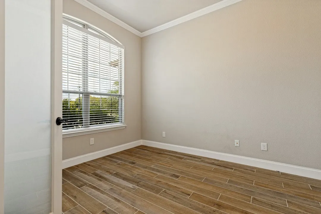 Arched window with blinds, wood-finish flooring, crown molding, white baseboards, and a solid door with a matte black handle