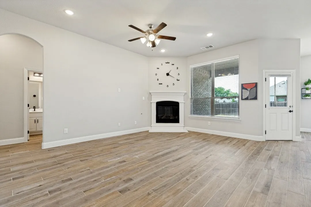 Spacious room featuring wood-finish flooring, a corner fireplace with a white mantel, recessed lighting, and an arched doorway. The entire main part of the home has the porcelain ceramic wood plank tile, very difficult to damage and a breeze to keep spotless.