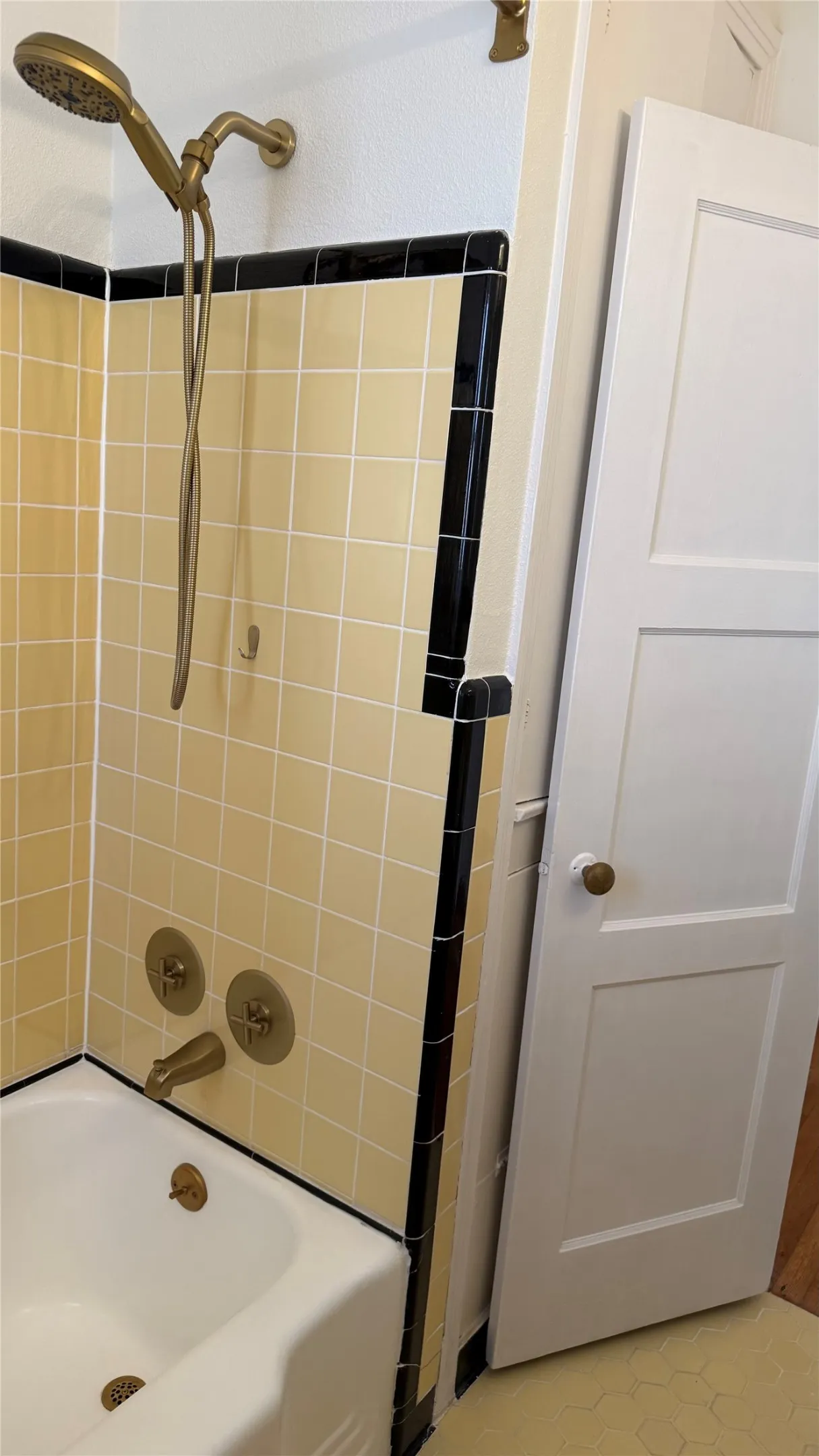 Bathtub with a shower fixture, square wall tiling, and a panel door