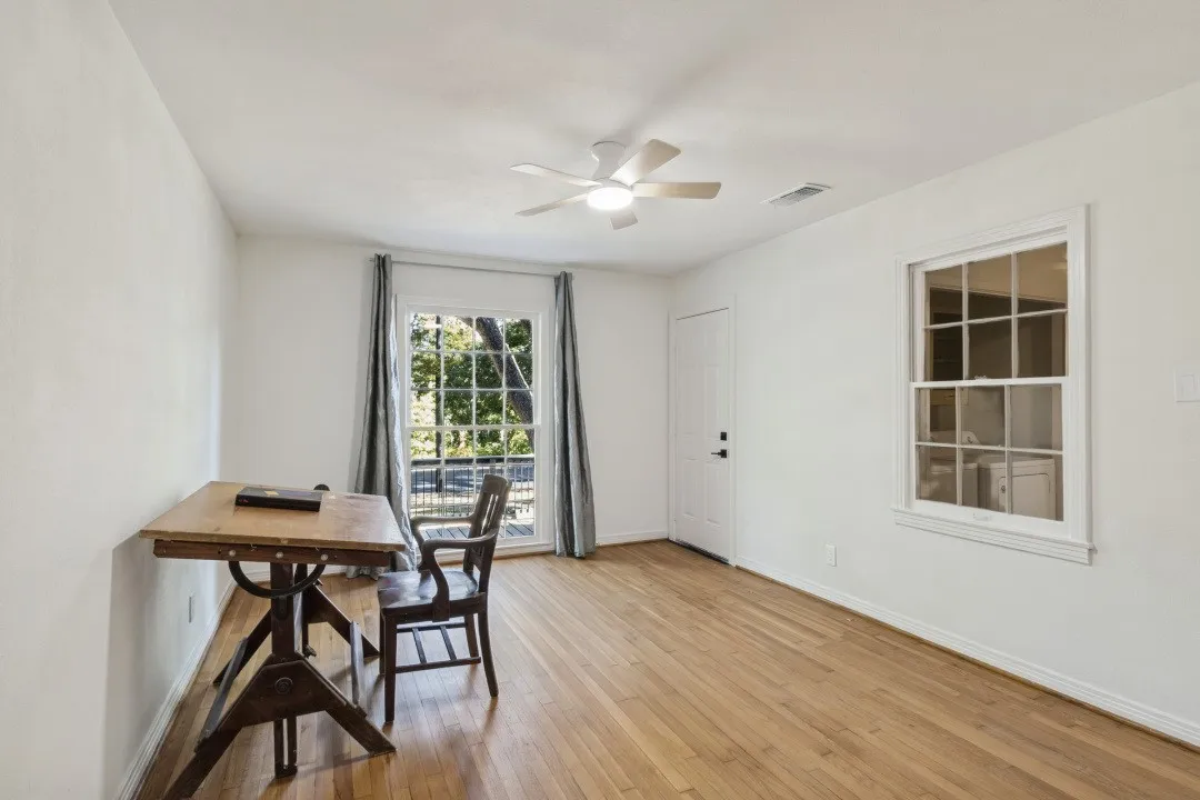 Hardwood flooring, ceiling fan, white paneled door, window with exterior lattice, second window with exterior lattice
