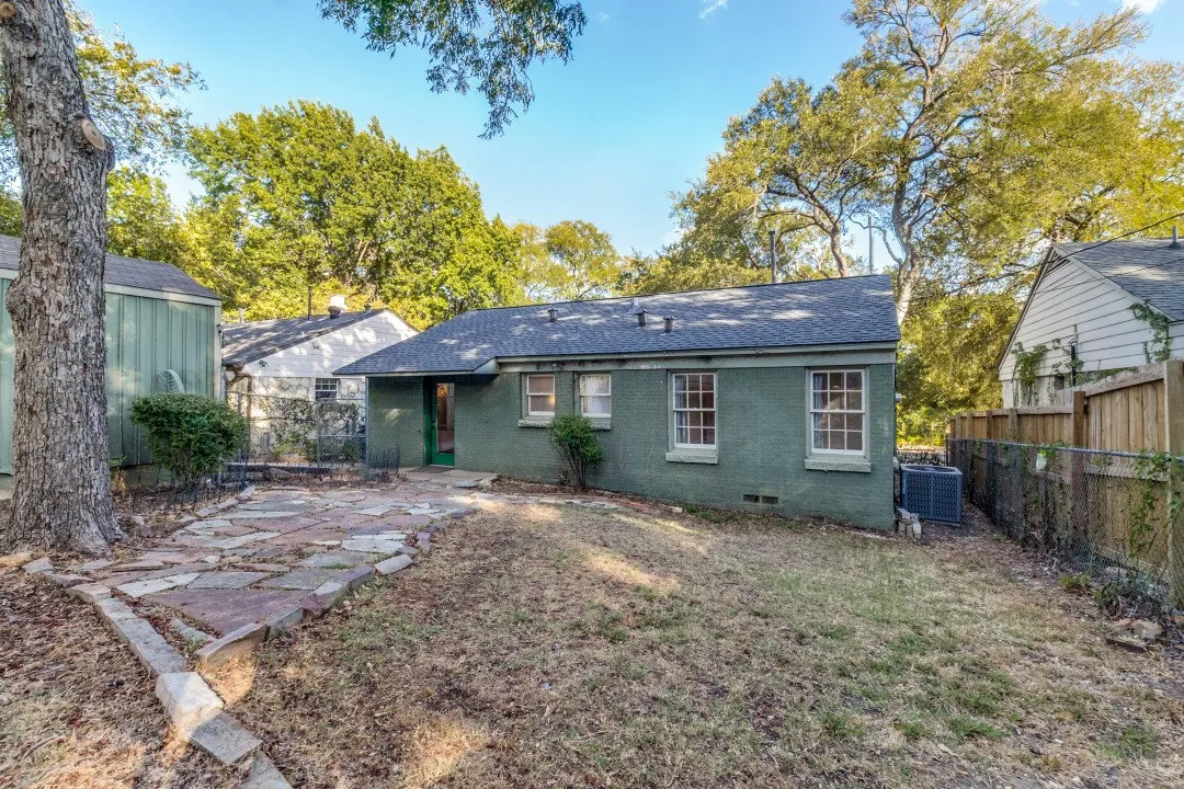 Rear exterior with a stone patio, mature trees, and a privacy fence