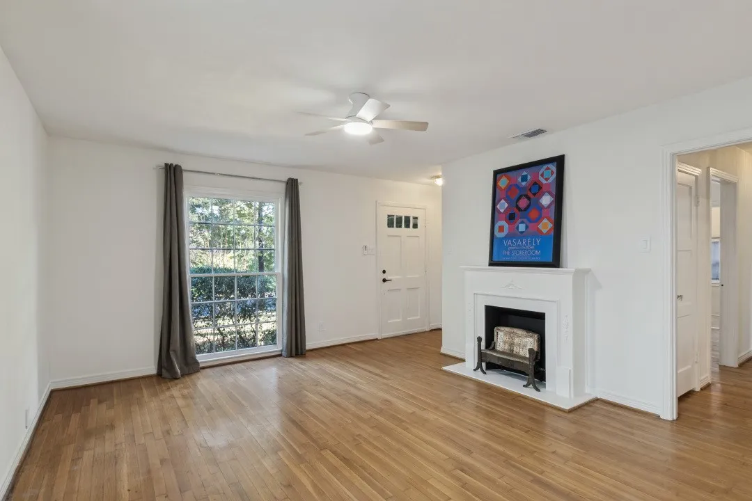 Hardwood flooring, white fireplace, ceiling fan, white paneled door, and large window