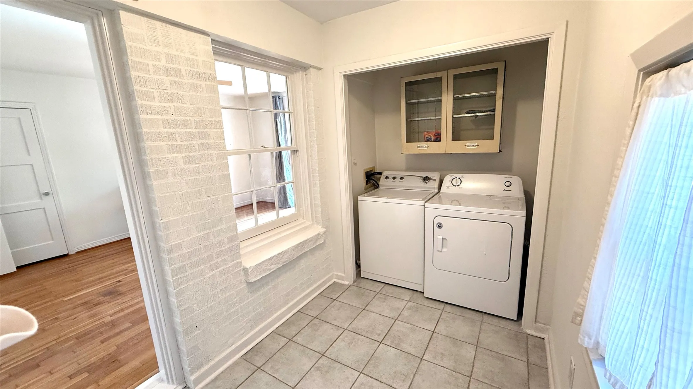 Laundry area featuring a tile floor, white brick wall detail, and built-in upper cabinetry