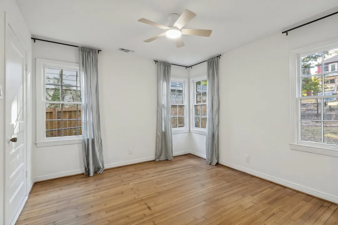 Wood-finish flooring, multiple windows, a ceiling fan with integrated lighting, and a paneled interior door