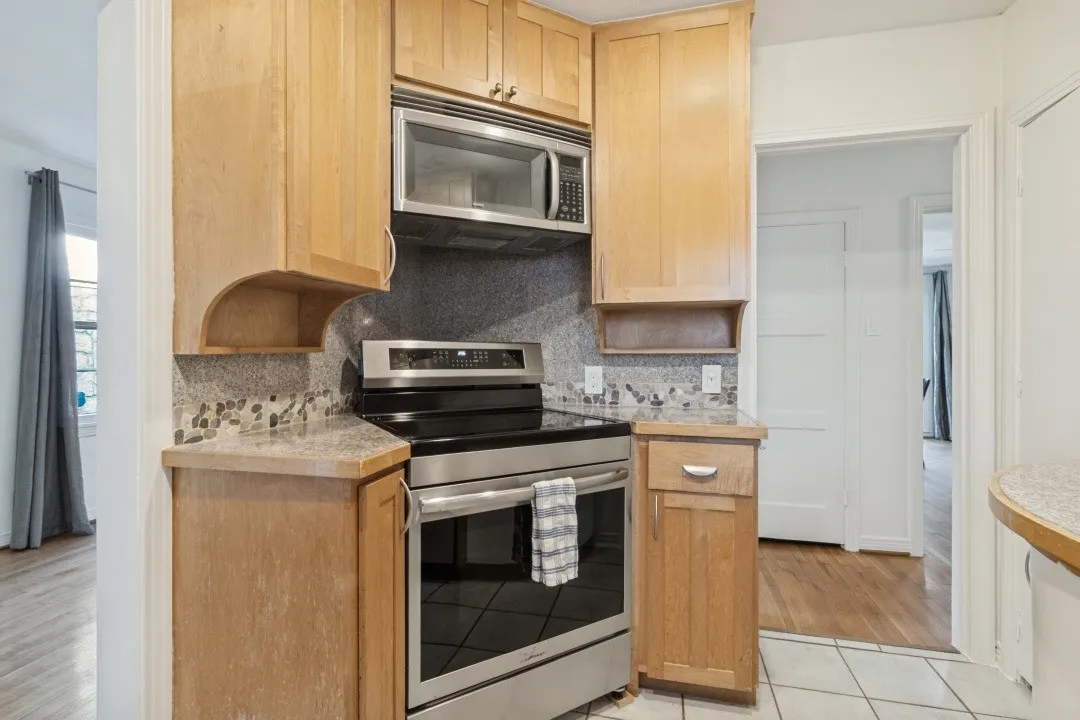 Wood cabinetry, stainless steel microwave, stainless steel range, patterned tile backsplash, and light-toned countertops