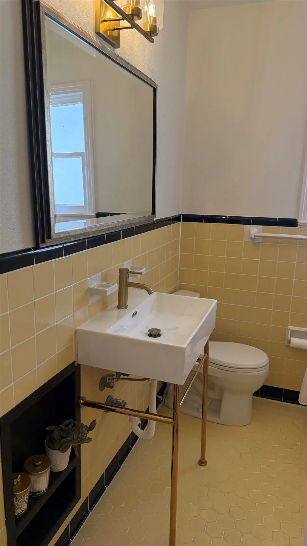 Rectangular wall-mounted mirror, modern vanity light fixture, yellow and black tiled walls, white rectangular vessel sink, and gold-finish plumbing fixtures