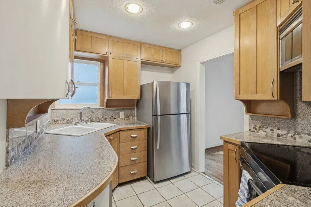 Kitchen featuring wood cabinetry, stainless steel appliances, granite-style countertops, mosaic tile backsplash, and tile flooring