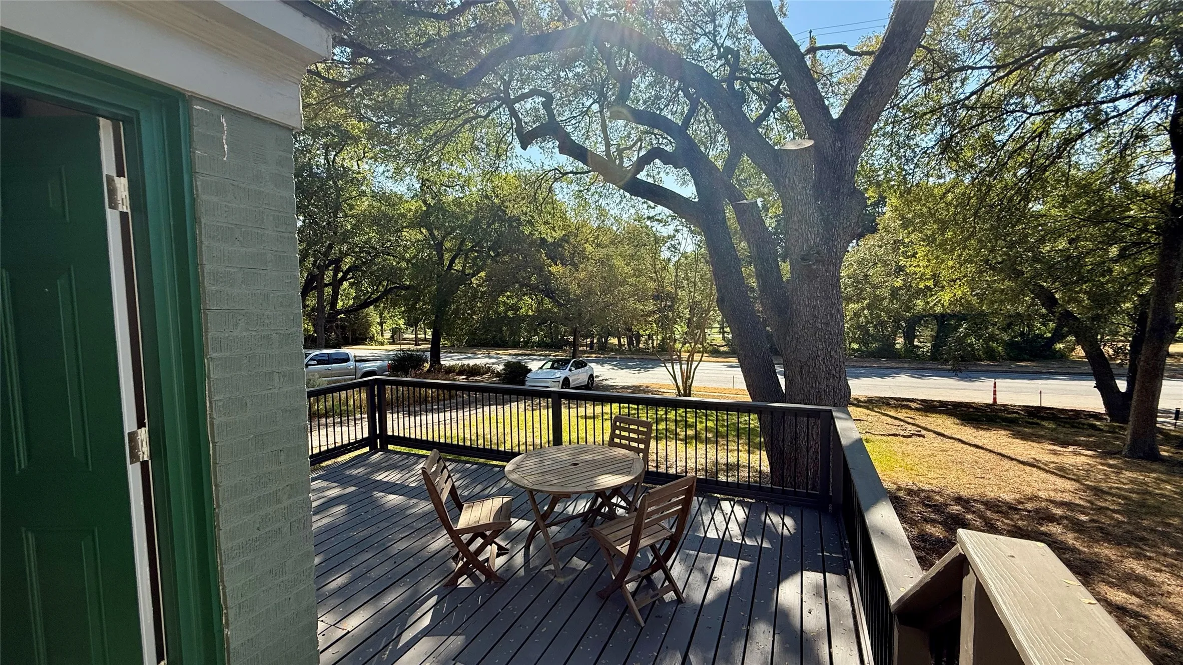 Spacious outdoor deck with dark wood-finish railing, overlooking mature trees and a paved road