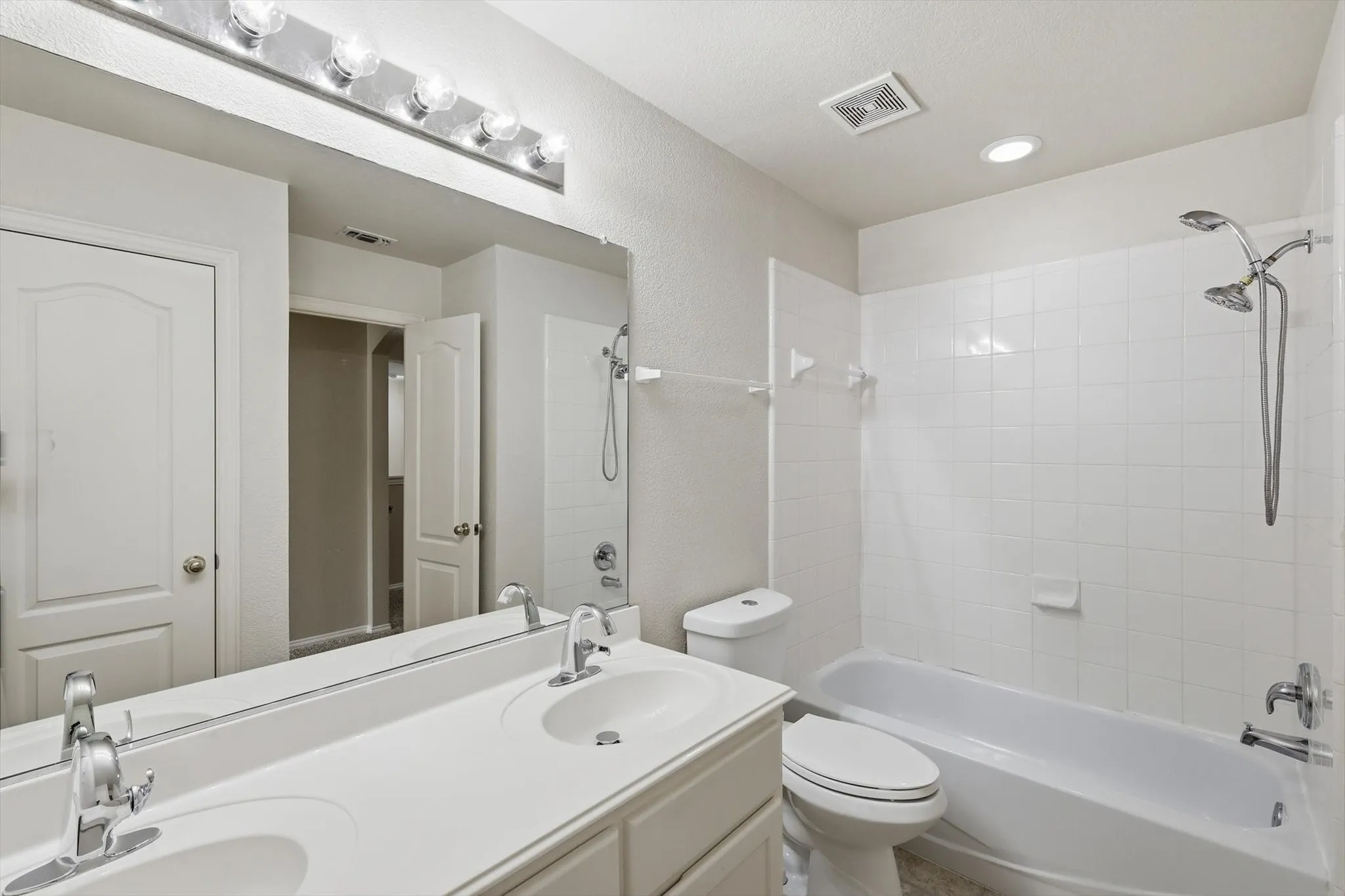 Upstairs Bathroom featuring a dual vanity with integrated sinks, a large wall-mounted mirror, and a white tiled shower-tub combination