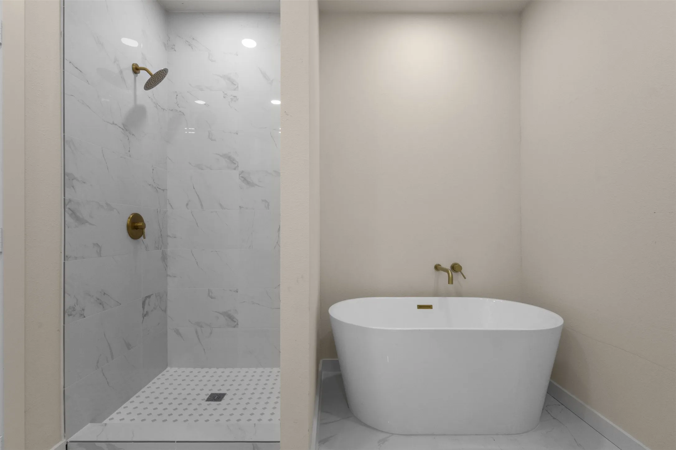 Freestanding soaking tub, walk-in shower with glass enclosure, white marble-look tile walls, and gold-finish fixtures