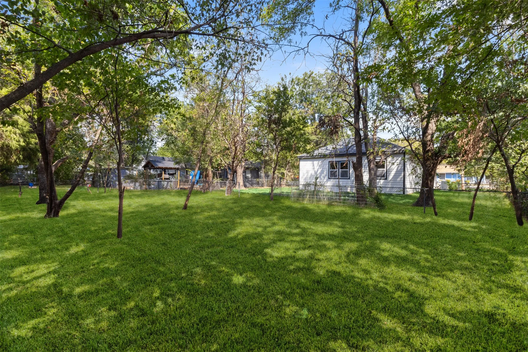 Expansive green lawn with mature trees and a single-story residence featuring light-colored siding