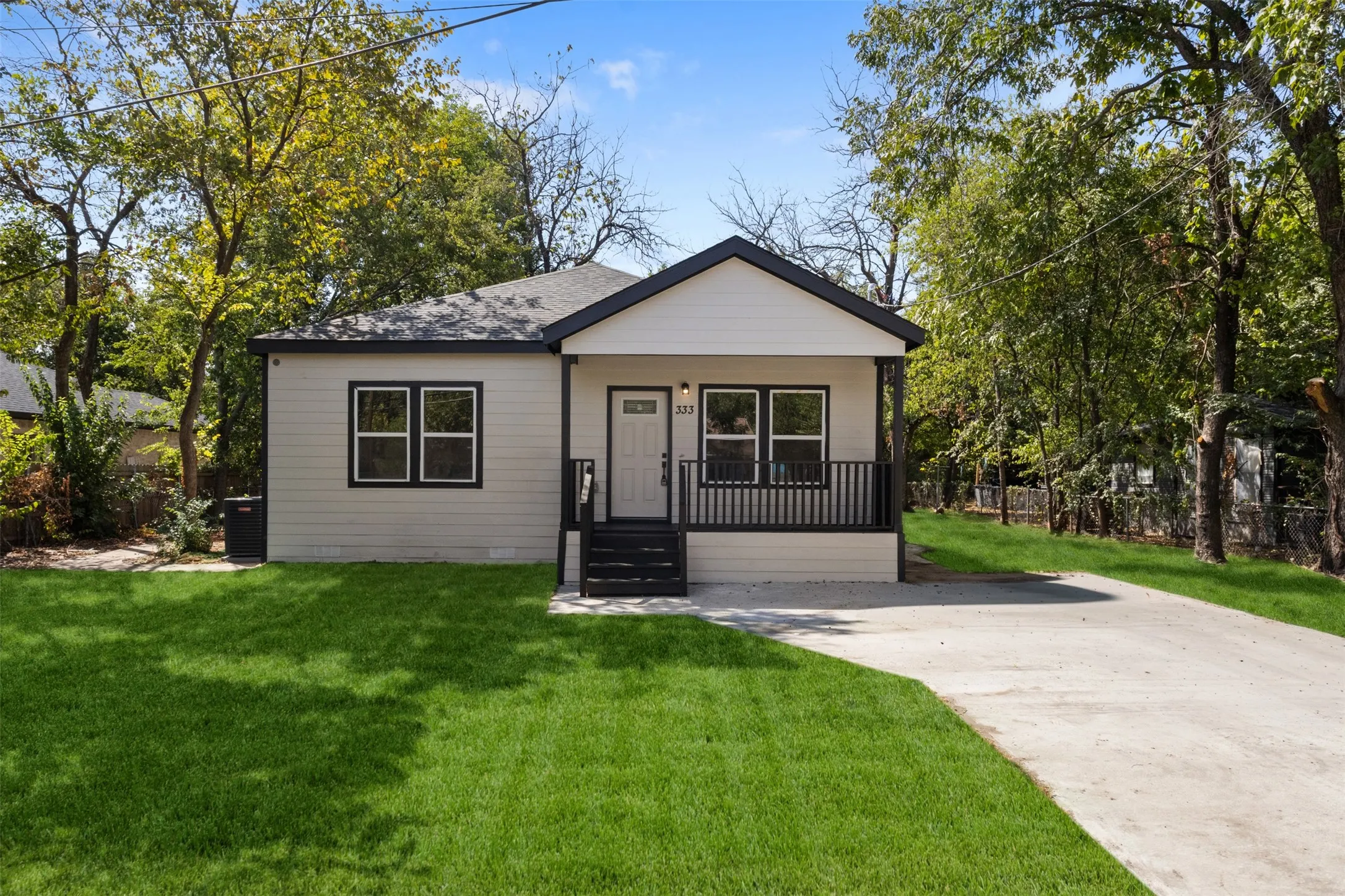 Light-toned siding exterior with dark trim accents, covered front porch, dark-railed steps, asphalt shingle roof, and a concrete driveway