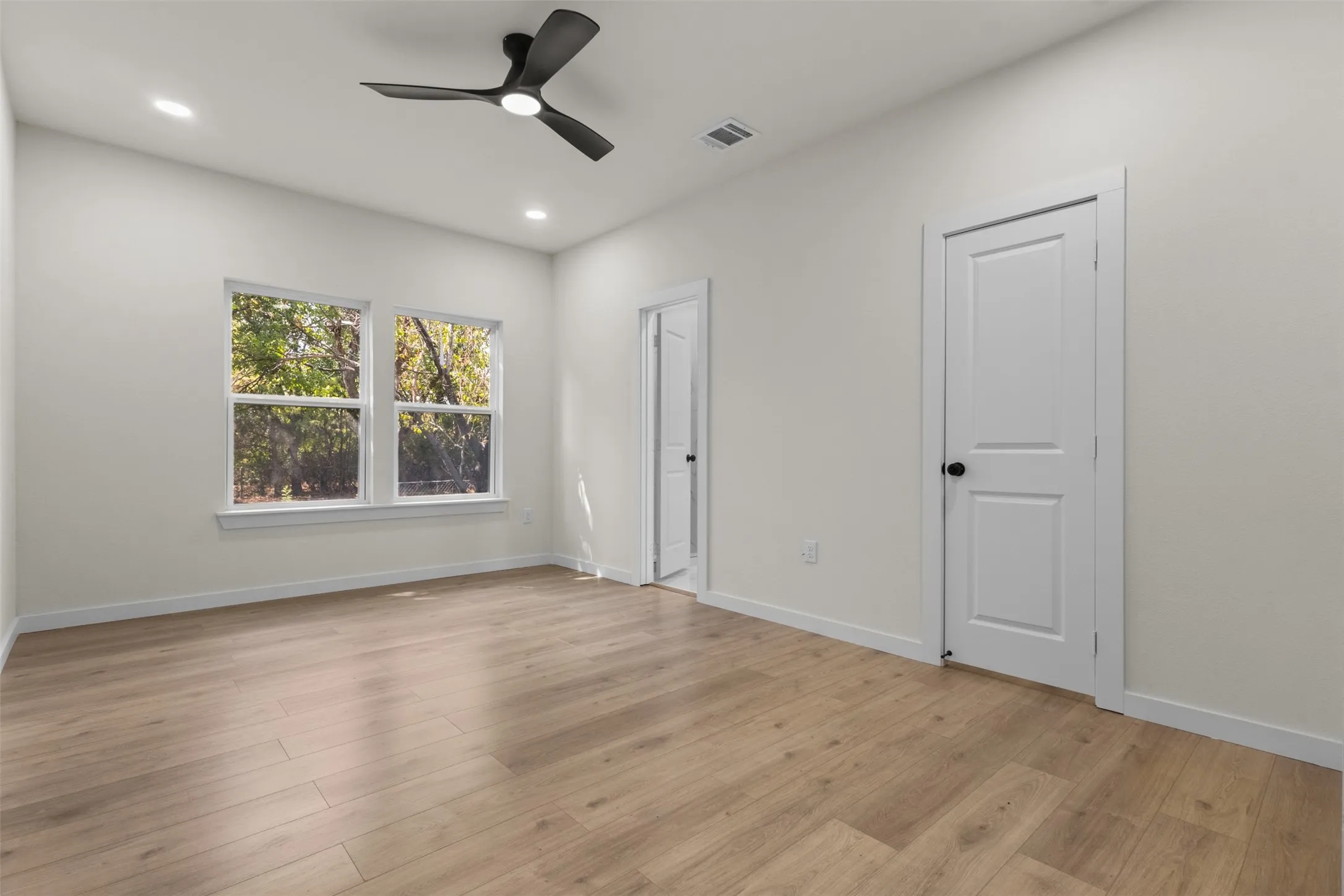 Light wood-finish flooring, white walls, and a modern ceiling fan with integrated lighting