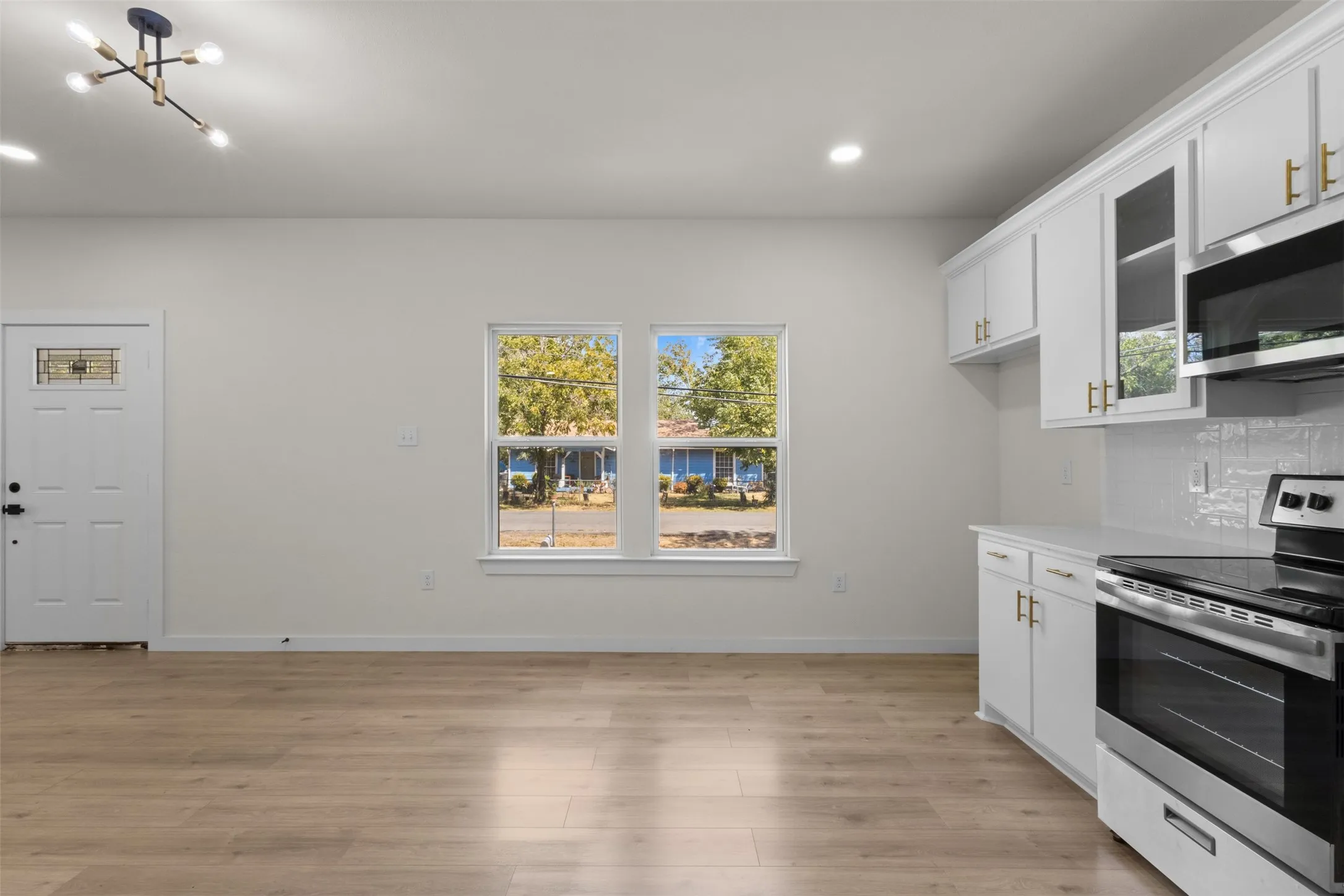 Wood-finish flooring, white cabinetry with gold-tone hardware, stainless steel range, built-in microwave, and recessed lighting
