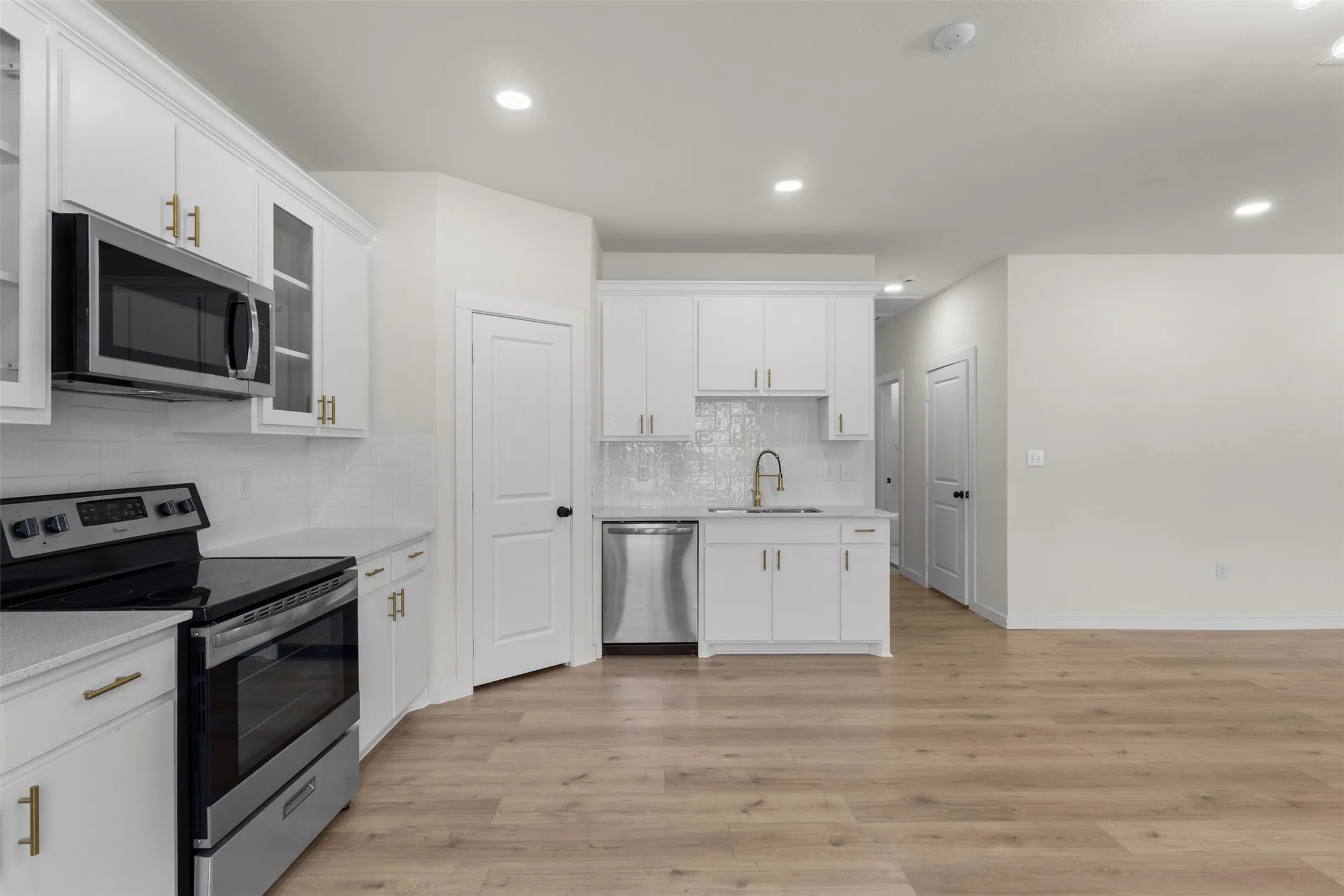 Kitchen featuring white cabinetry with gold-finish hardware, stainless steel appliances, white subway tile backsplash, and light wood-finish flooring