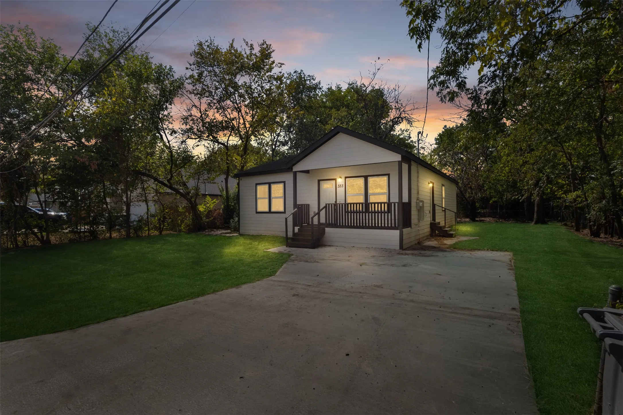 White exterior siding with dark trim, covered front porch, concrete driveway, manicured lawn, and mature trees