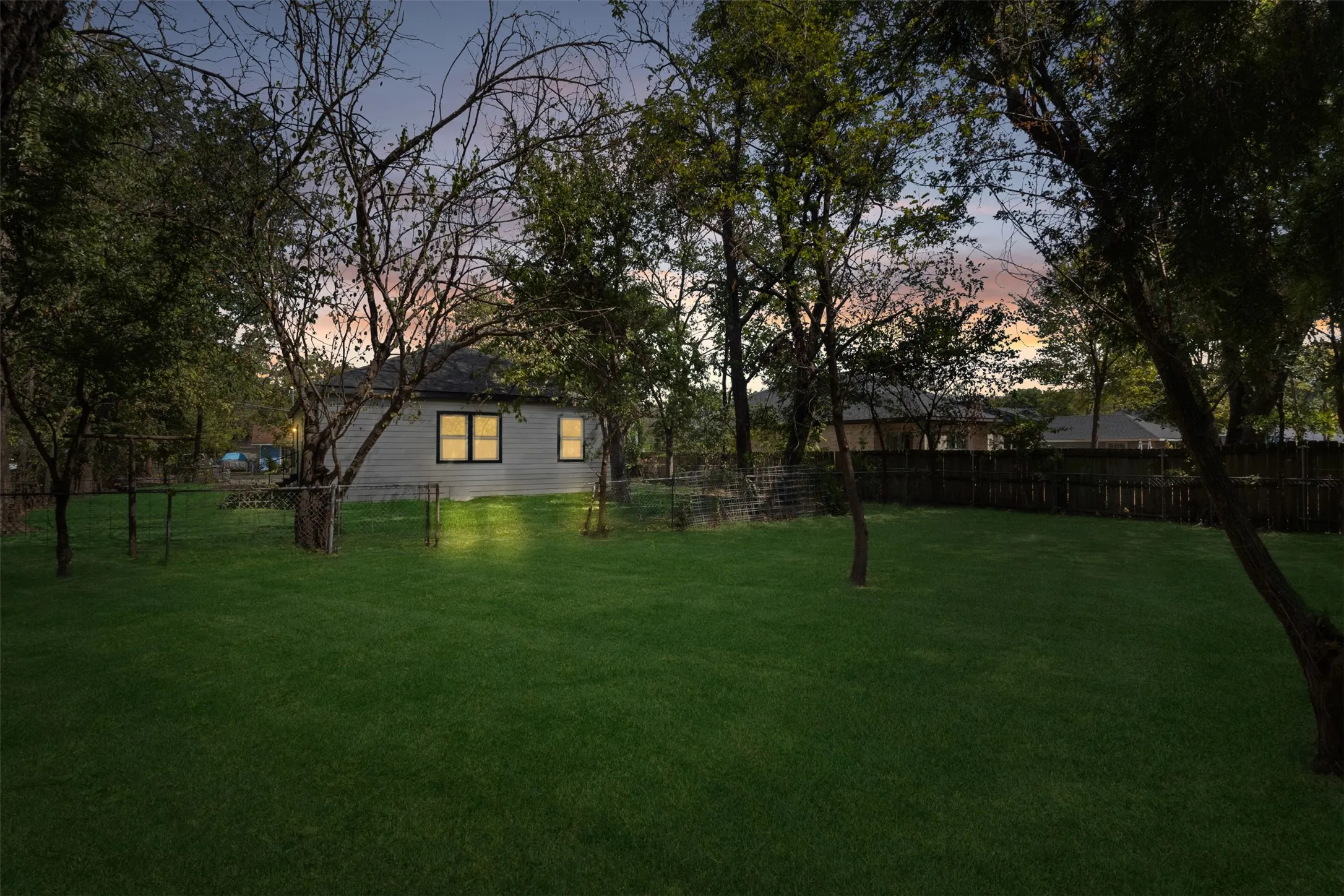 Expansive rear yard featuring a manicured lawn, established trees, and perimeter fencing