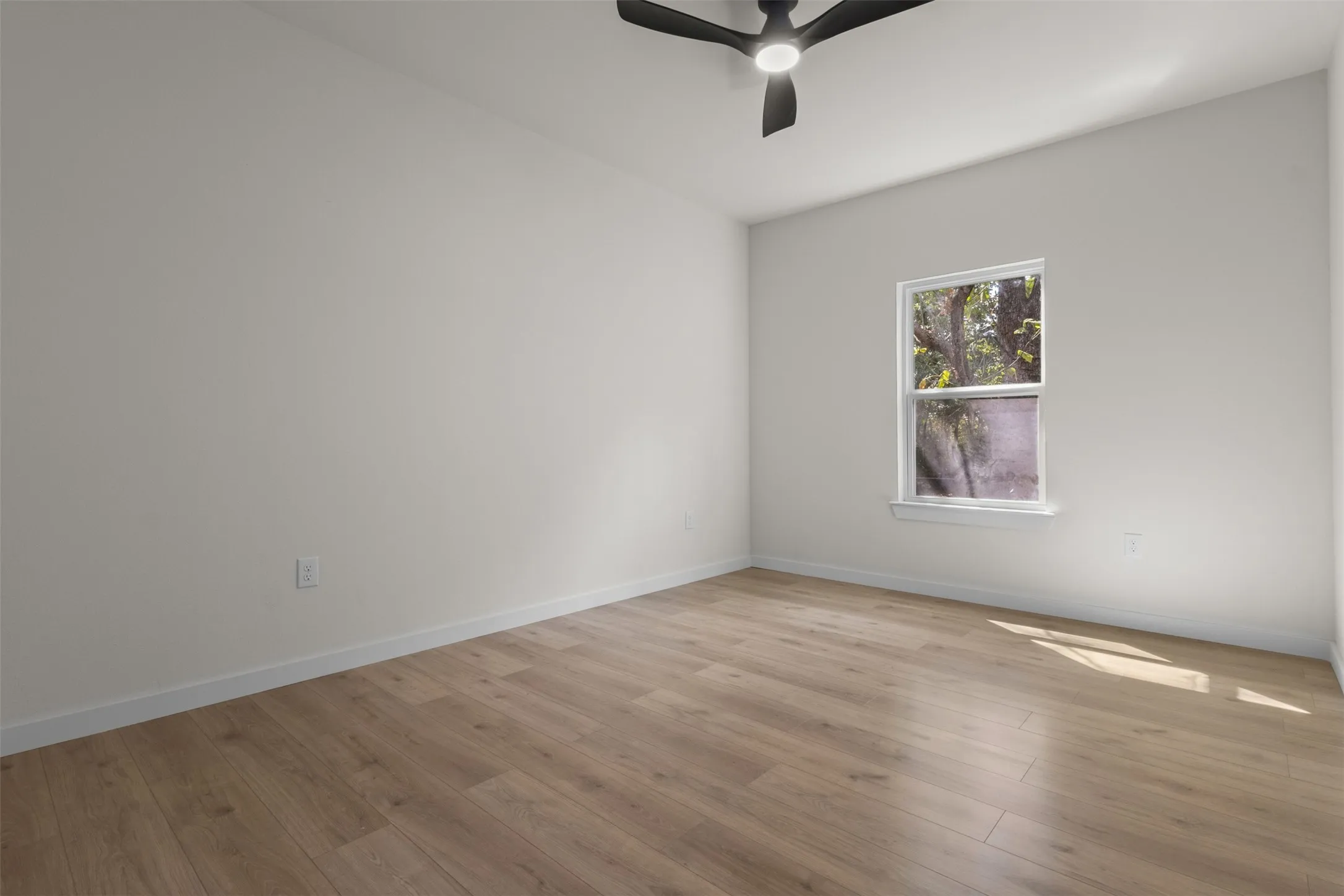 Neutral wall color, wood-finish flooring, single window, white trim, and a ceiling fan