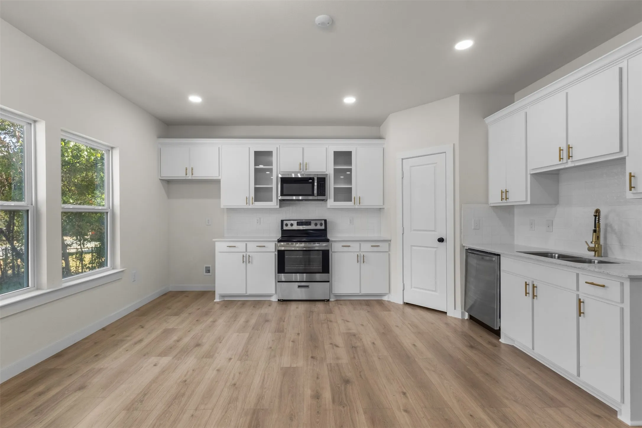 Spacious kitchen with wood-finish flooring, white cabinetry, stainless steel appliances, and recessed lighting