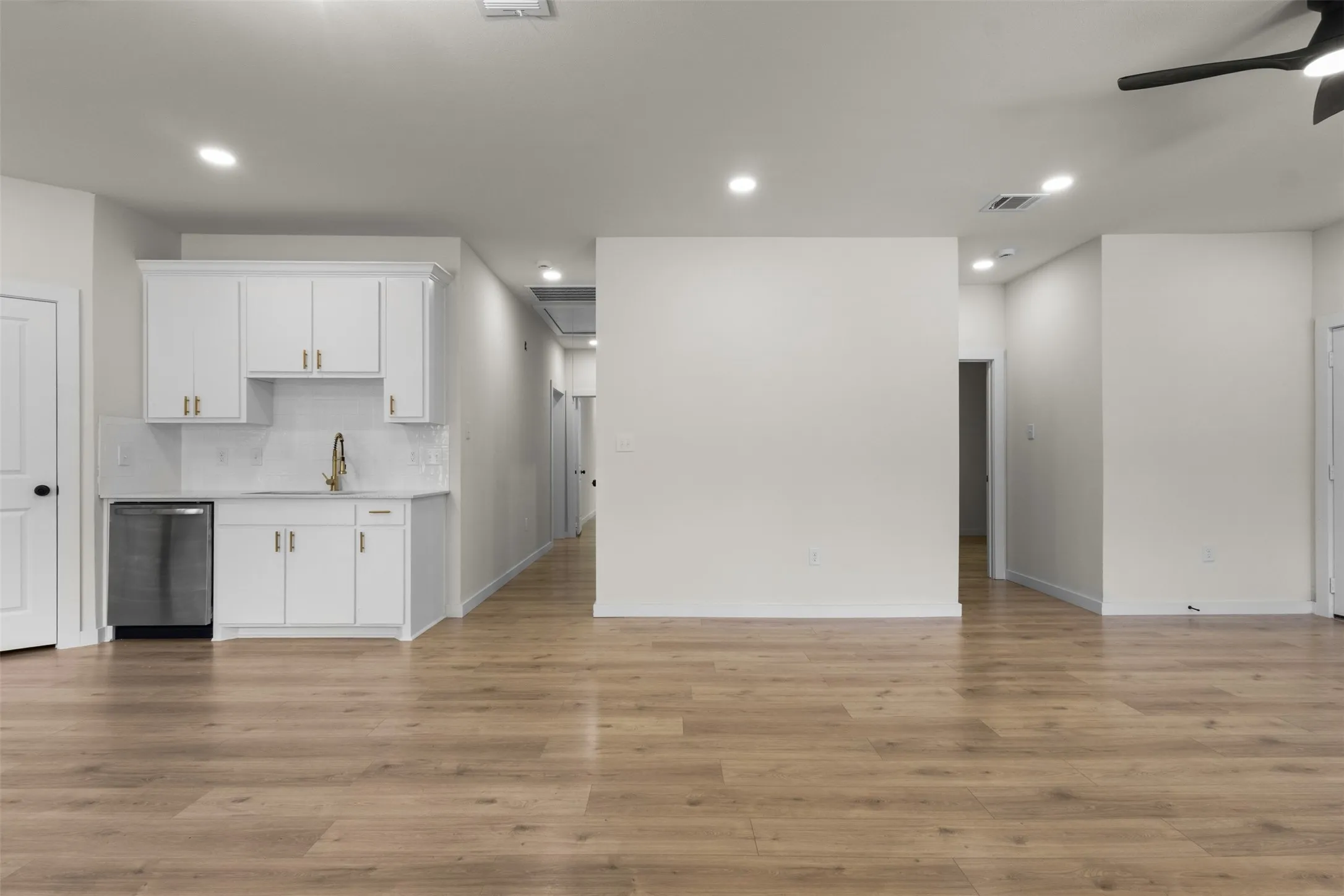 Wood-finish flooring, recessed lighting, ceiling fan, white cabinetry with gold-tone hardware, and a stainless steel dishwasher