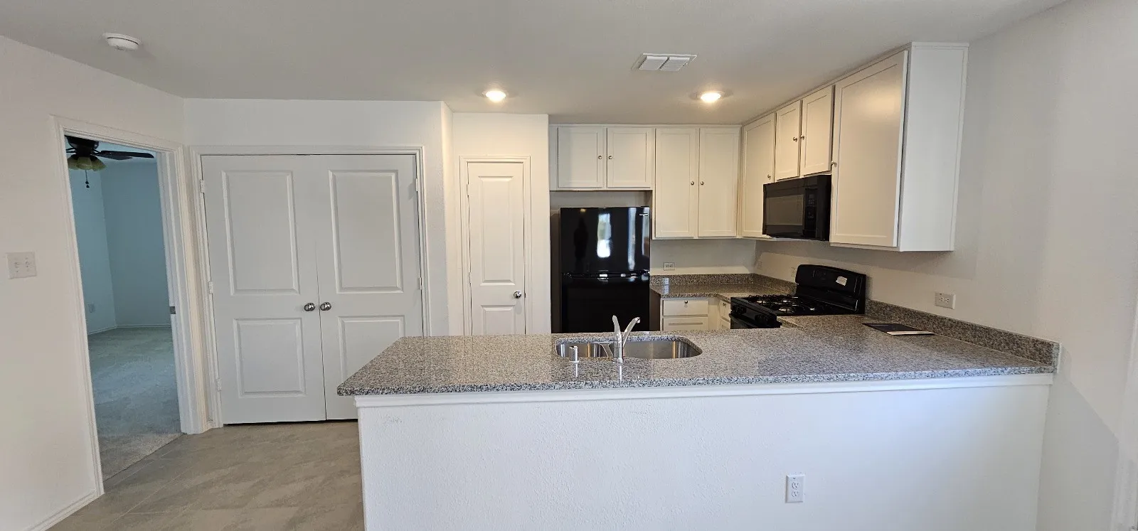 Kitchen featuring black appliances, light stone counters, white cabinets, a peninsula, and recessed lighting