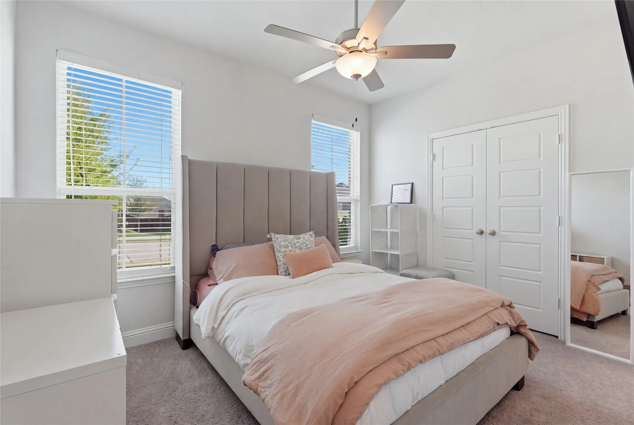 Carpeted room featuring a ceiling fan with integrated lighting, two windows with blinds, and white bi-fold closet doors
