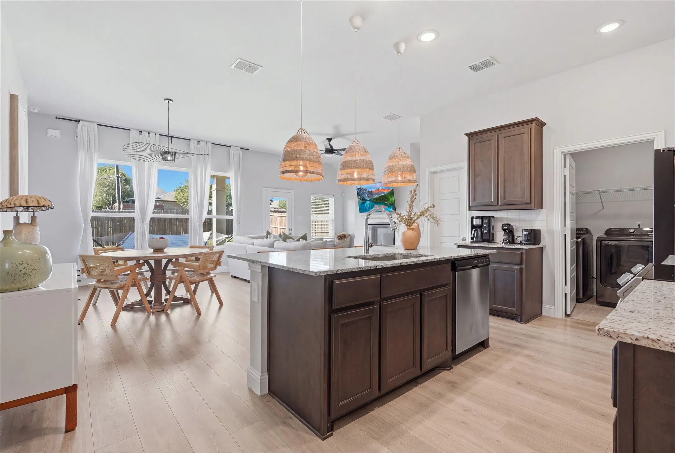 Open-concept living space with light wood-finish flooring, a kitchen island featuring a granite-style countertop, dark wood cabinetry, and stainless steel appliances