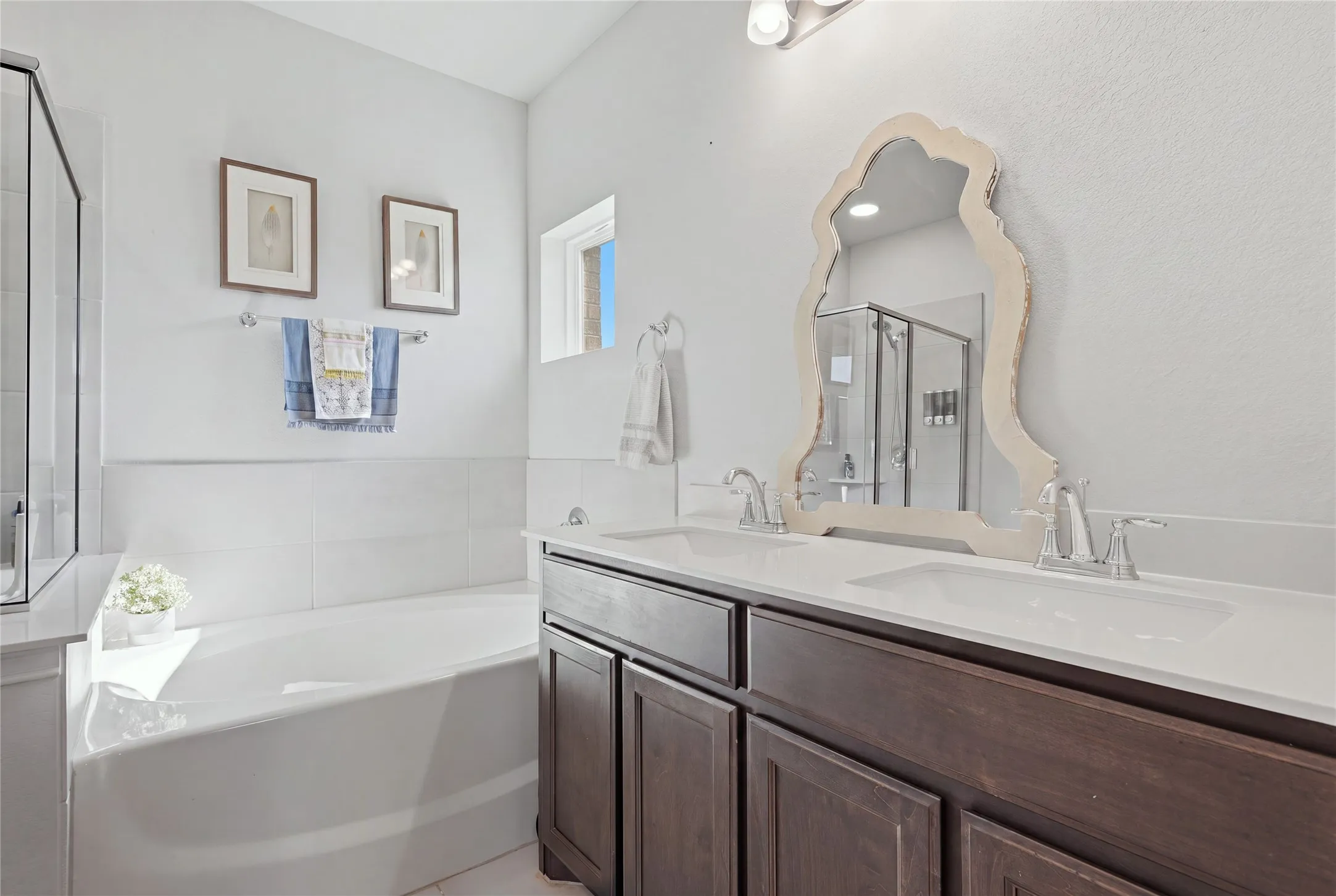 Dual vanity with undermount sinks and chrome fixtures, framed mirror, built-in bathtub with white tile surround, and a clear glass enclosed shower