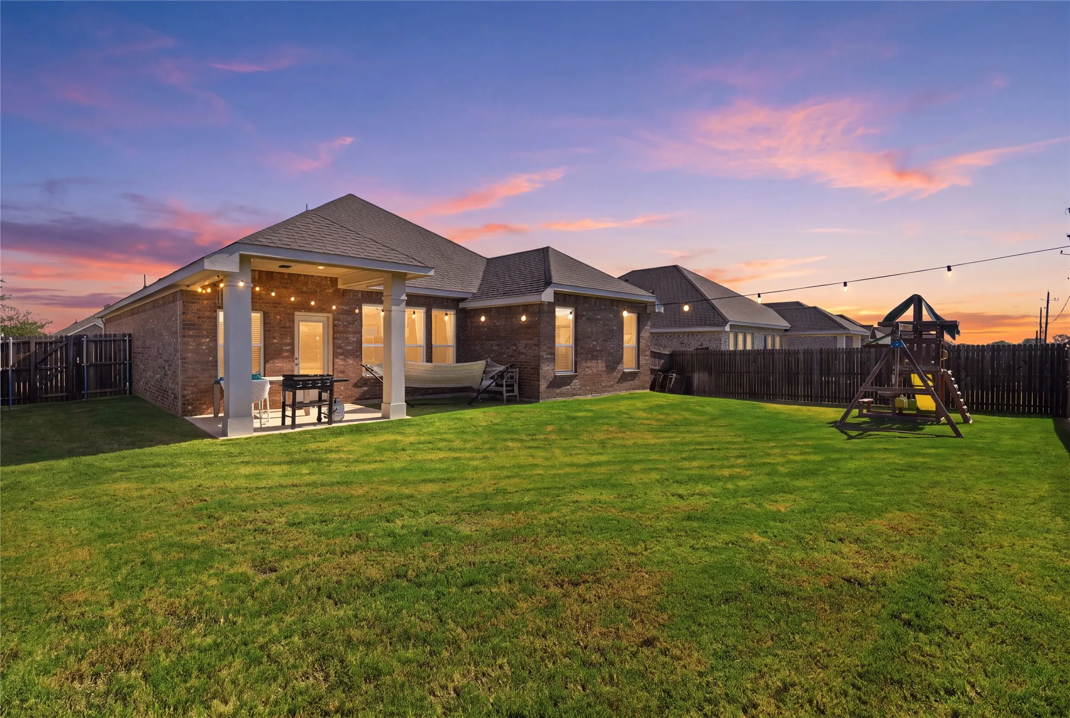 Brick exterior with a covered patio, extensive lawn, and a privacy fence
