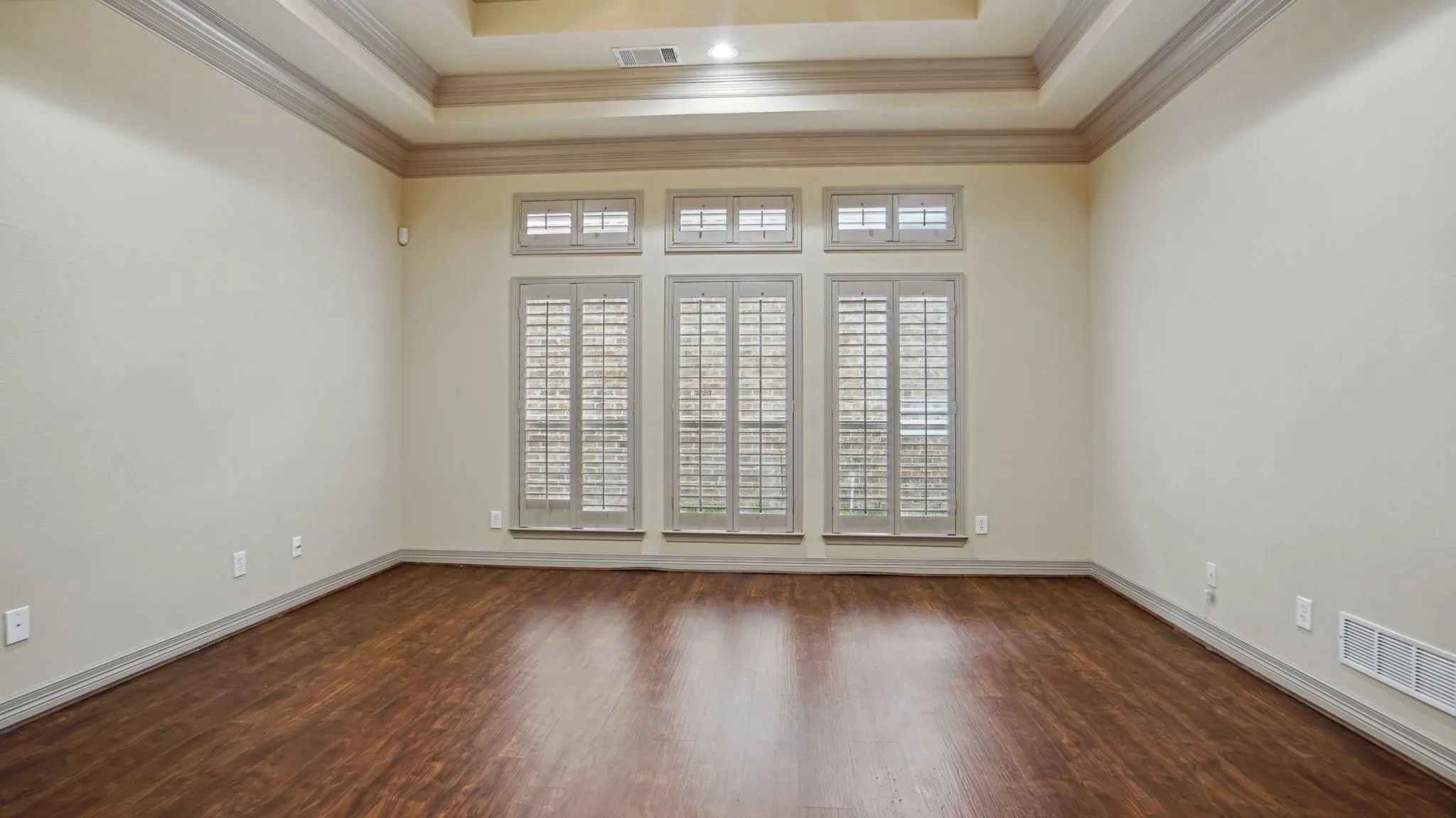 Empty room with crown molding, a raised ceiling, wood finished floors, and visible vents
