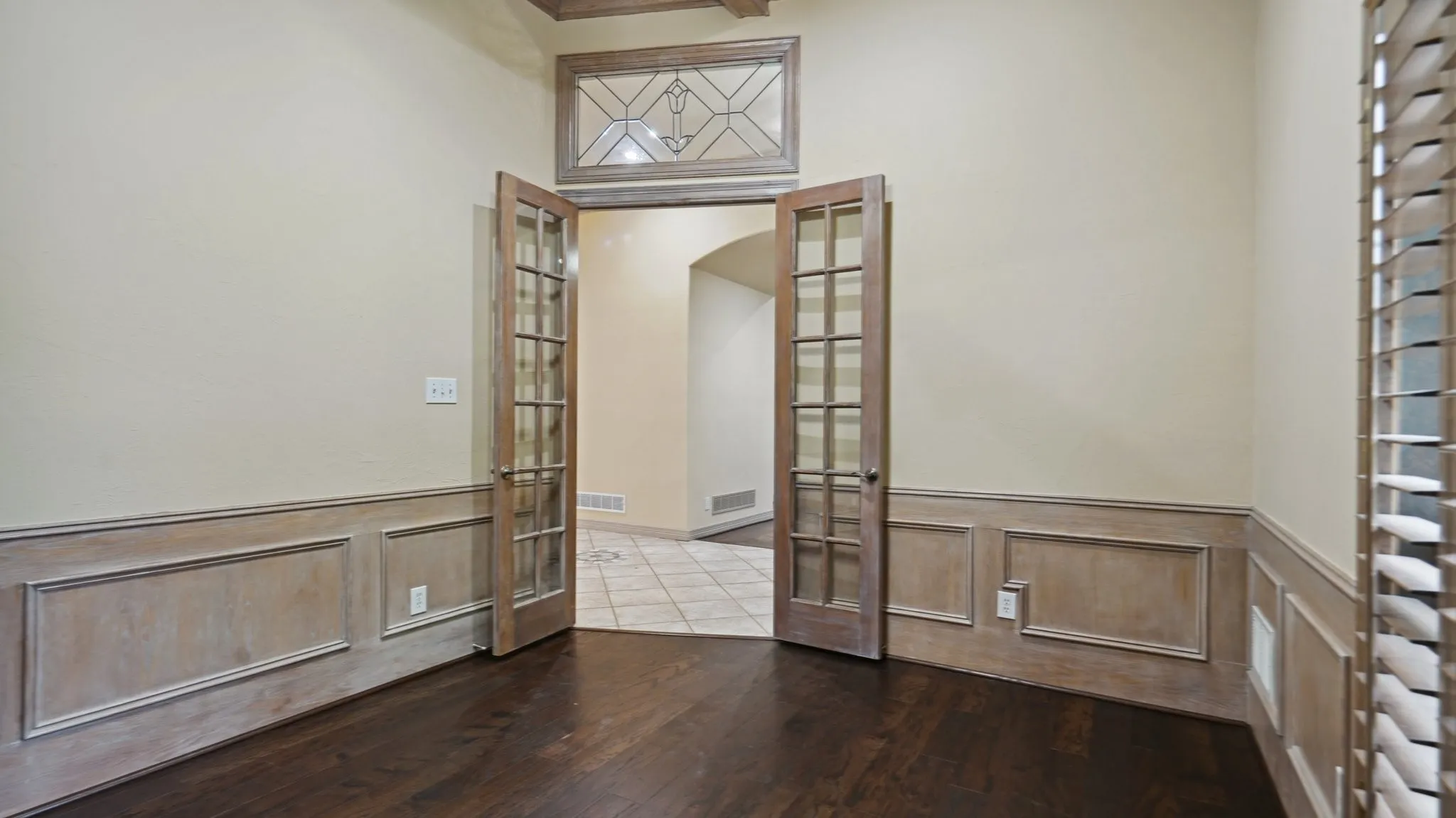Empty room with a wainscoted wall, visible vents, french doors, and dark wood-type flooring