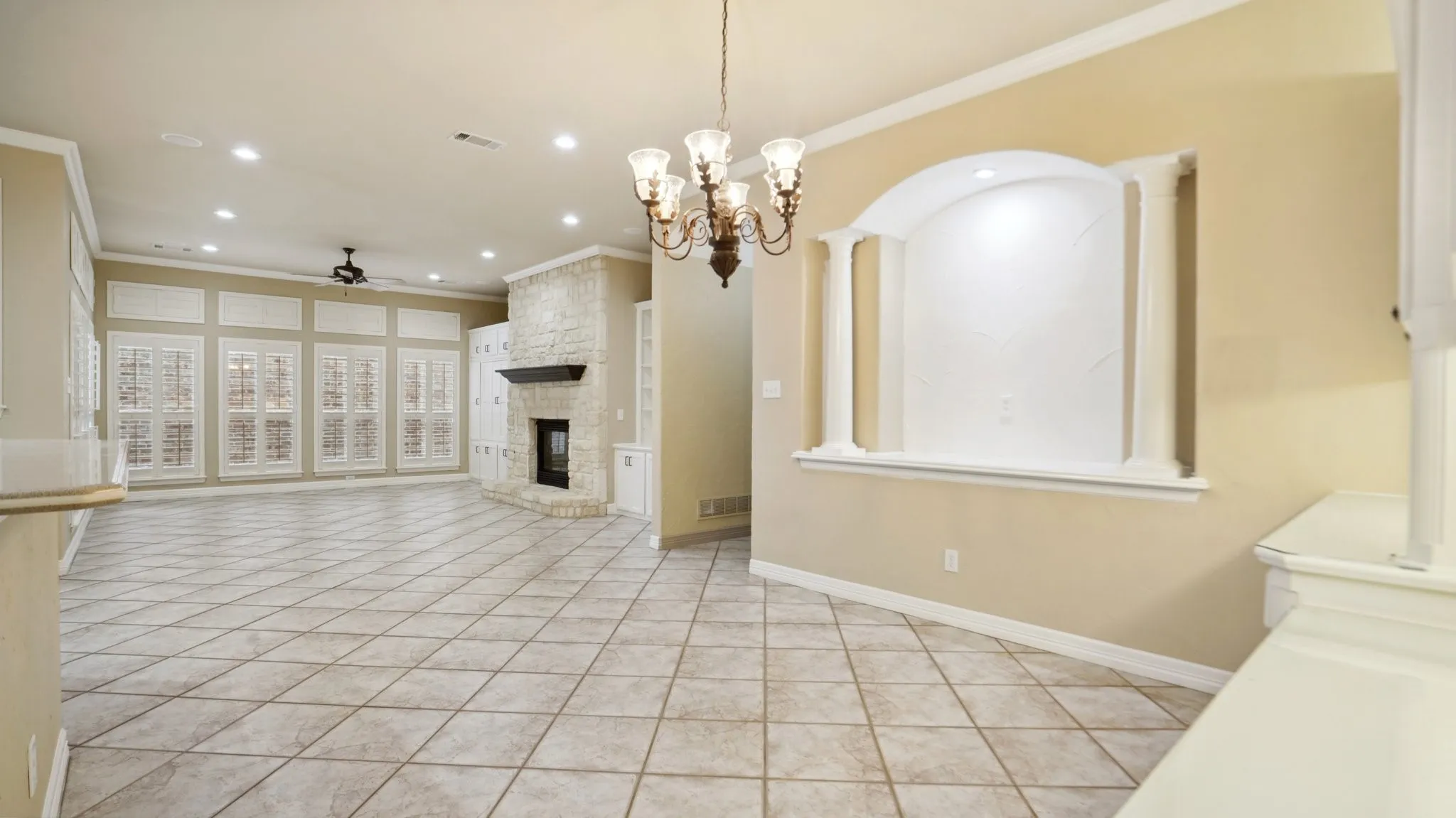 Unfurnished living room with ceiling fan with notable chandelier, recessed lighting, light tile patterned floors, visible vents, and ornamental molding