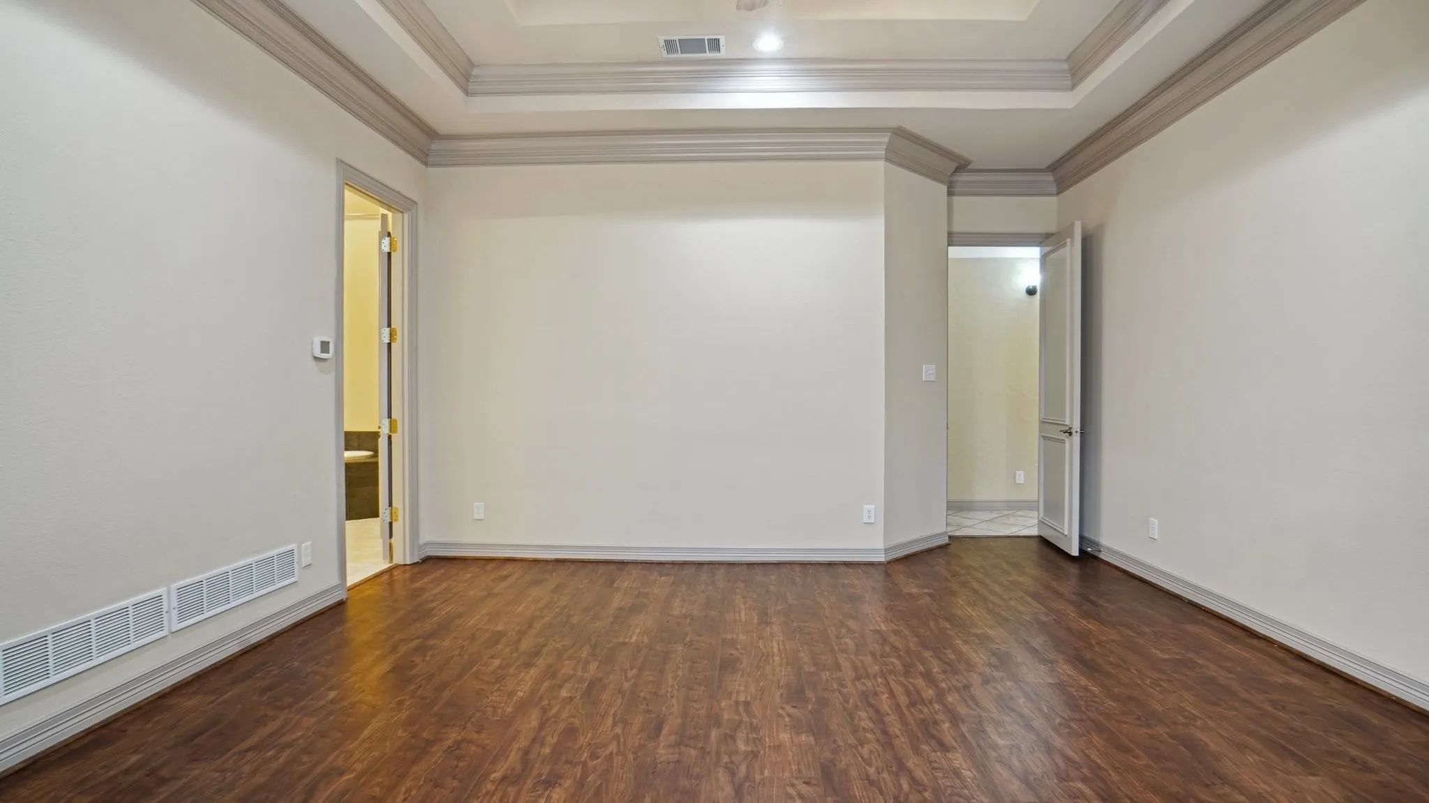Empty room featuring a raised ceiling, ornamental molding, wood finished floors, and visible vents