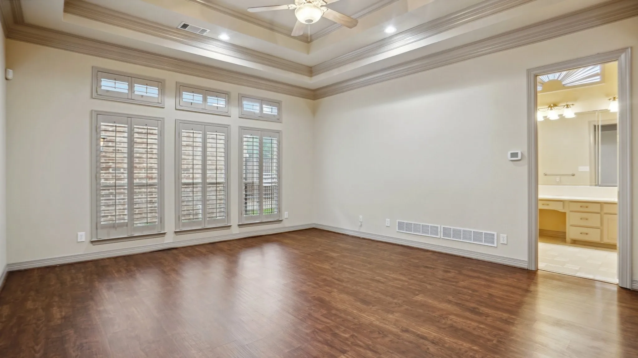 Spare room featuring crown molding, a ceiling fan, wood finished floors, a tray ceiling, and visible vents