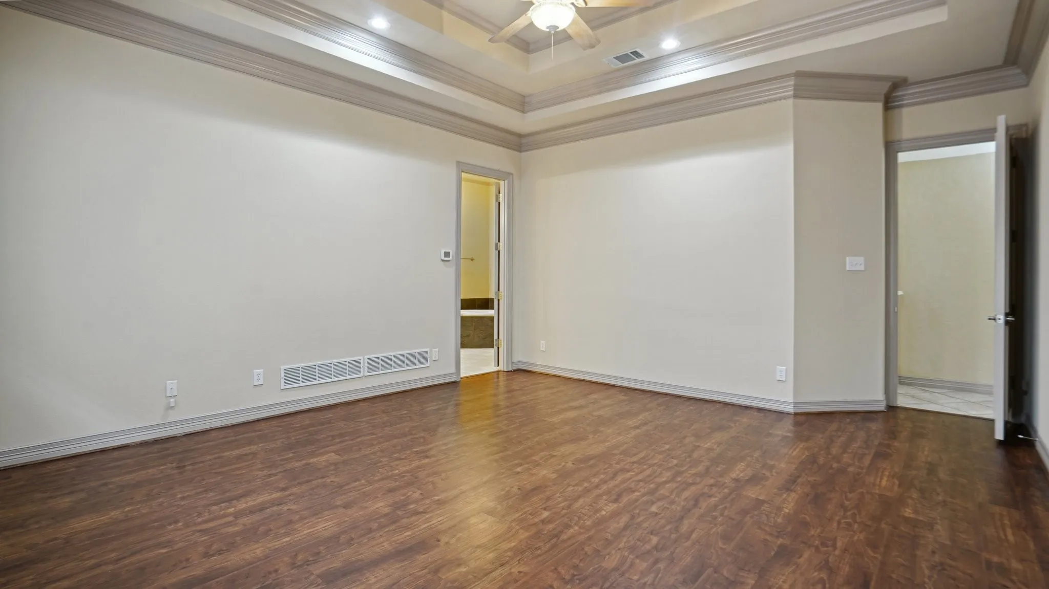 Empty room featuring crown molding, visible vents, wood finished floors, and a raised ceiling