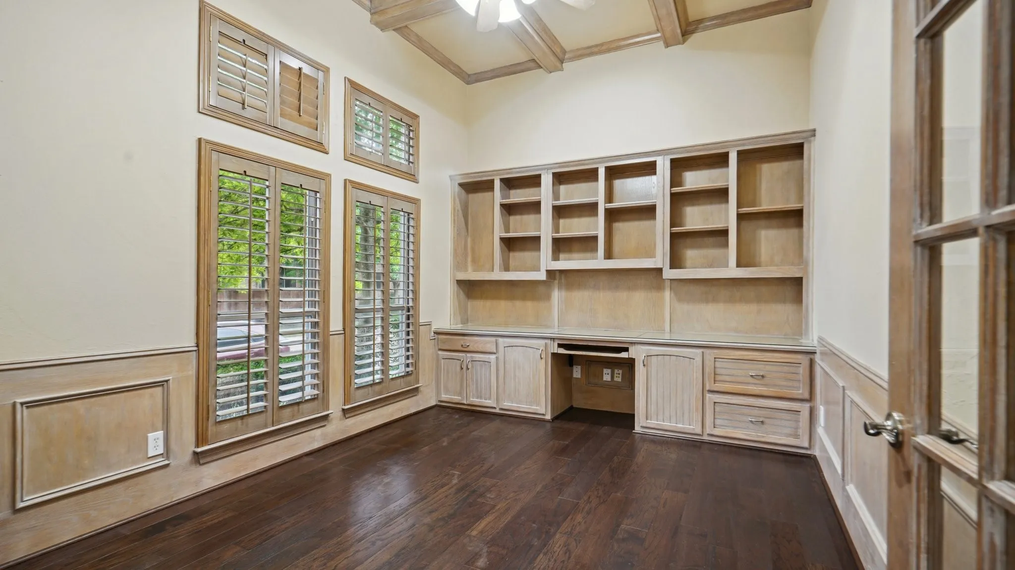 Unfurnished office featuring ceiling fan, dark wood-style flooring, wainscoting, built in study area, and beamed ceiling