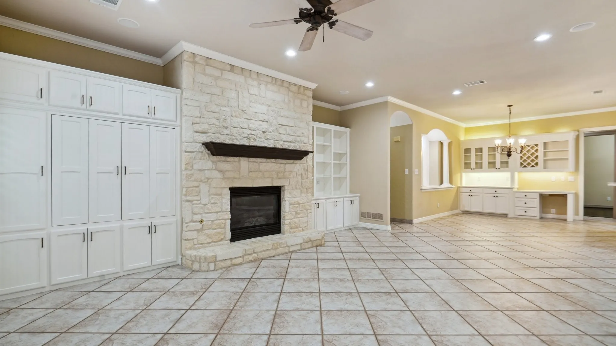 Unfurnished living room with ornamental molding, ceiling fan with notable chandelier, recessed lighting, and a stone fireplace